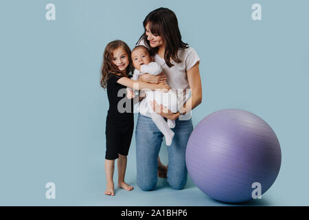 Family Portrait einer Mutter mit zwei Töchtern neben einem Yoga Ball über Blau Stockfoto