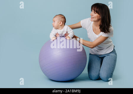 Glückliche Mutter Übungen mit Ihrem Kleinkind Baby auf lila Yoga ball Stockfoto