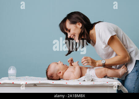 Mutter ändern Windel auf Ihrem Baby am Tisch über blauen Hintergrund. Stockfoto