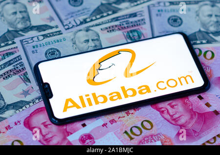 Alibaba com-Logo auf dem Bildschirm des Smartphones auf dem US-Dollar und Yuan Banknoten platziert. Konzept für internationale Handelsunternehmen Alibaba Stockfoto