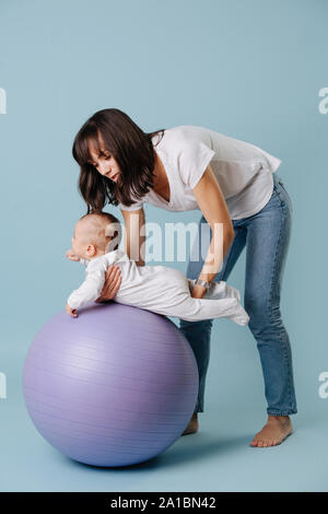 Glückliche Mutter Übungen mit Ihrem Kleinkind Baby auf lila Yoga ball Stockfoto