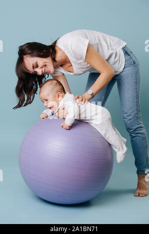 Glückliche Mutter Übungen mit Ihrem Kleinkind Baby auf lila Yoga ball Stockfoto