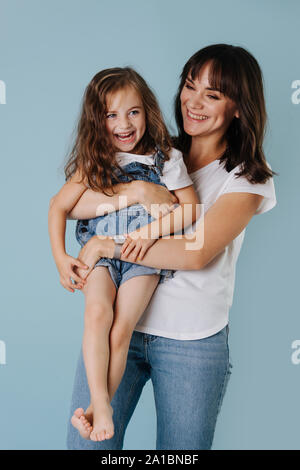 Mutter hält ihre Tochter auf Händen nach außen über blauer Hintergrund Stockfoto
