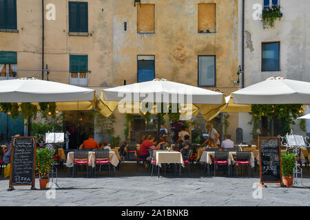 Restaurant im Freien an der Piazza dell'Anfiteatro im Zentrum von Lucca mit Menschen und Touristen zu Mittag essen, unter Sonnenschirmen im Sommer, Toskana, Italien Stockfoto
