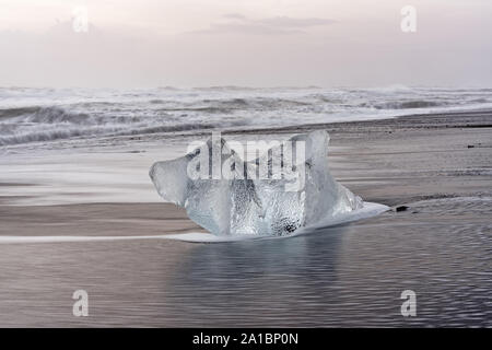 Markante Eisblock auf einem schwarzen Strand mit Surf, mit wieder Wasser Reflexion auf dem nassen Sand, Wellen im Hintergrund rolling - Ort: Island Stockfoto