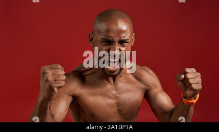 Stärker mit jedem neuen Tag. Nahaufnahme eines afrikanischen Mannes, der vor der Kamera schreit, während er vor rotem Hintergrund steht. Fitness und Workout Konzept. Motivation Stockfoto