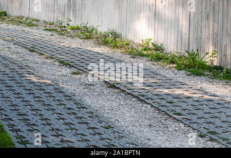 Geschwungene Straße bergauf mit Kies und Rasengittersteine neben konkreten Garten Wand gelegt Stockfoto