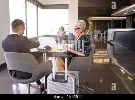 Lächelnd diverse Kollegen in der modernen Lounge im Flughafen sitzen mit Gepäck entwickeln Geschäftsideen zusammen Stockfoto