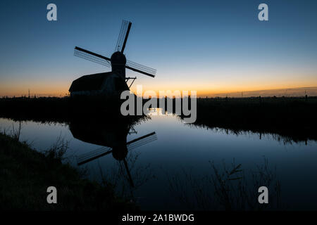 Silhouette einer traditionellen holländischen Windmühle gegen den Abendhimmel. Die Mühle ist im Wasser, in einem nahe gelegenen Bach wider. Stockfoto