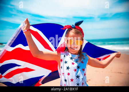 Gerne britische Mädchen trägt flattern Blau Weiß Rot Flagge von Großbritannien, des Vereinigten Königreichs und Nordirland gegen den blauen Himmel und das Meer zurück Stockfoto