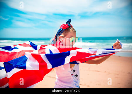 Gerne britische Mädchen trägt flattern Blau Weiß Rot Flagge von Großbritannien, des Vereinigten Königreichs und Nordirland gegen den blauen Himmel und das Meer zurück Stockfoto
