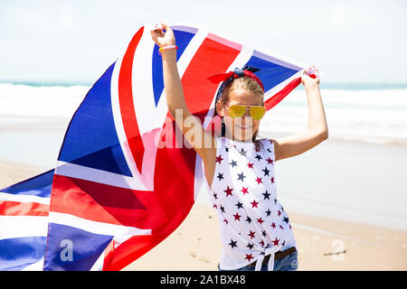 Gerne britische Mädchen trägt flattern Blau Weiß Rot Flagge von Großbritannien, des Vereinigten Königreichs und Nordirland gegen den blauen Himmel und das Meer zurück Stockfoto
