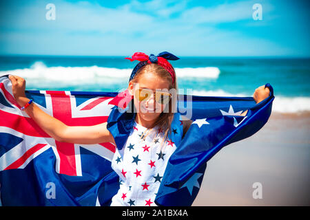 Gerne australische Mädchen trägt flattern Blau Weiß Rot Australische Flagge gegen den blauen Himmel und Ozean Hintergrund Stockfoto