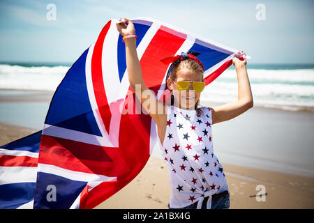Gerne britische Mädchen trägt flattern Blau Weiß Rot Flagge von Großbritannien, des Vereinigten Königreichs und Nordirland gegen den blauen Himmel und das Meer zurück Stockfoto