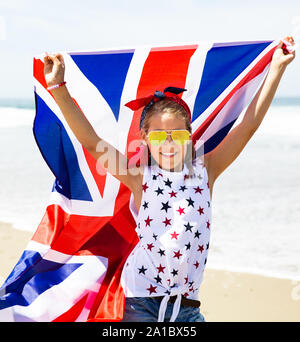 Gerne britische Mädchen trägt flattern Blau Weiß Rot Flagge von Großbritannien, des Vereinigten Königreichs und Nordirland gegen den blauen Himmel und das Meer zurück Stockfoto