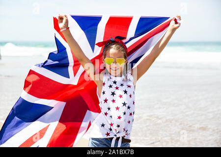 Gerne britische Mädchen trägt flattern Blau Weiß Rot Flagge von Großbritannien, des Vereinigten Königreichs und Nordirland gegen den blauen Himmel und das Meer zurück Stockfoto
