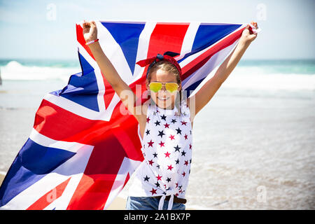 Gerne britische Mädchen trägt flattern Blau Weiß Rot Flagge von Großbritannien, des Vereinigten Königreichs und Nordirland gegen den blauen Himmel und das Meer zurück Stockfoto