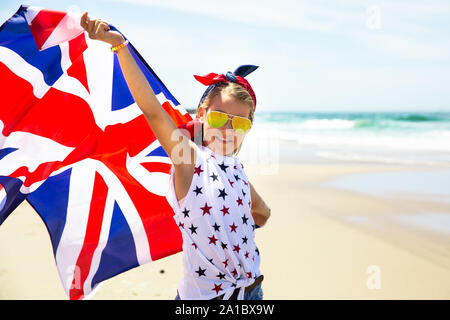 Gerne britische Mädchen trägt flattern Blau Weiß Rot Flagge von Großbritannien, des Vereinigten Königreichs und Nordirland gegen den blauen Himmel und das Meer zurück Stockfoto