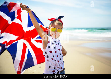 Gerne britische Mädchen trägt flattern Blau Weiß Rot Flagge von Großbritannien, des Vereinigten Königreichs und Nordirland gegen den blauen Himmel und das Meer zurück Stockfoto