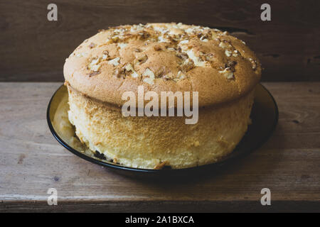 Baumwollschwammkuchen mit Walnüssen oben und Rosinen (getrocknete schwarze Trauben) unten, verzehrfertig, auf rustikalem Holztisch, hausgemacht. Vintage getont Stockfoto