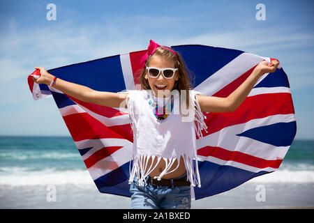 Gerne britische Mädchen trägt flattern Blau Weiß Rot Flagge von Großbritannien, des Vereinigten Königreichs und Nordirland gegen den blauen Himmel und das Meer zurück Stockfoto
