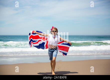 Gerne britische Mädchen trägt flattern Blau Weiß Rot Flagge von Großbritannien, des Vereinigten Königreichs und Nordirland gegen den blauen Himmel und das Meer zurück Stockfoto
