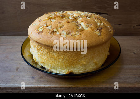 Baumwollschwammkuchen mit Walnüssen oben und Rosinen (getrocknete schwarze Trauben) unten, verzehrfertig, auf rustikalem Holztisch, hausgemacht Stockfoto