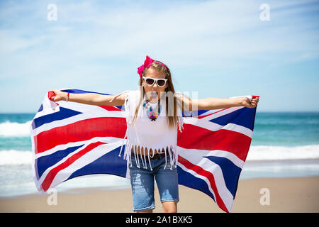 Gerne britische Mädchen trägt flattern Blau Weiß Rot Flagge von Großbritannien, des Vereinigten Königreichs und Nordirland gegen den blauen Himmel und das Meer zurück Stockfoto