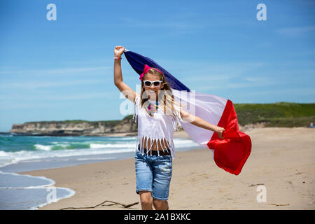 Gerne französische Mädchen trägt flattern Blau Weiß Rot französische Flagge Frankreichs gegen den blauen Himmel und den Atlantik Hintergrund Stockfoto