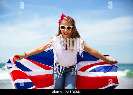 Gerne britische Mädchen trägt flattern Blau Weiß Rot Flagge von Großbritannien, des Vereinigten Königreichs und Nordirland gegen den blauen Himmel und das Meer zurück Stockfoto