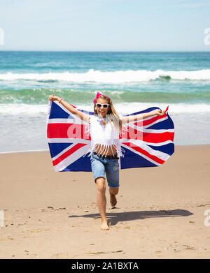 Gerne britische Mädchen trägt flattern Blau Weiß Rot Flagge von Großbritannien, des Vereinigten Königreichs und Nordirland gegen den blauen Himmel und das Meer zurück Stockfoto