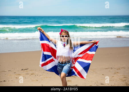 Gerne britische Mädchen trägt flattern Blau Weiß Rot Flagge von Großbritannien, des Vereinigten Königreichs und Nordirland gegen den blauen Himmel und das Meer zurück Stockfoto