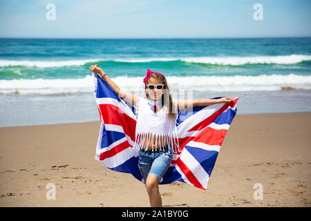 Gerne britische Mädchen trägt flattern Blau Weiß Rot Flagge von Großbritannien, des Vereinigten Königreichs und Nordirland gegen den blauen Himmel und das Meer zurück Stockfoto