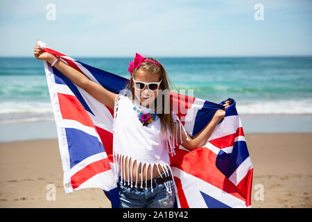 Gerne britische Mädchen trägt flattern Blau Weiß Rot Flagge von Großbritannien, des Vereinigten Königreichs und Nordirland gegen den blauen Himmel und das Meer zurück Stockfoto