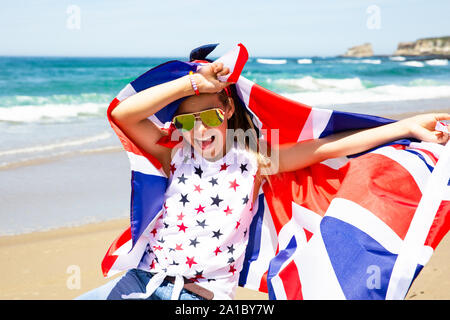 Gerne britische Mädchen trägt flattern Blau Weiß Rot Flagge von Großbritannien, des Vereinigten Königreichs und Nordirland gegen den blauen Himmel und das Meer zurück Stockfoto