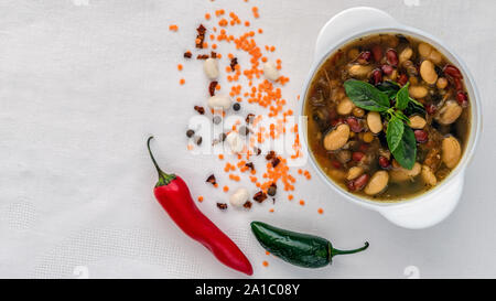 Mexikanische Suppe der sieben Arten von Bohnen, Nahaufnahme, auf einem weißen Hintergrund durch rote und grüne Paprika und Bohnen umgeben Stockfoto