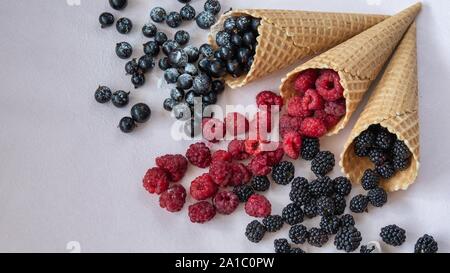 Blick von oben auf die drei Waffeln aus, die auf dem Tisch Himbeeren, Johannisbeeren, Brombeeren in Puderzucker Stockfoto