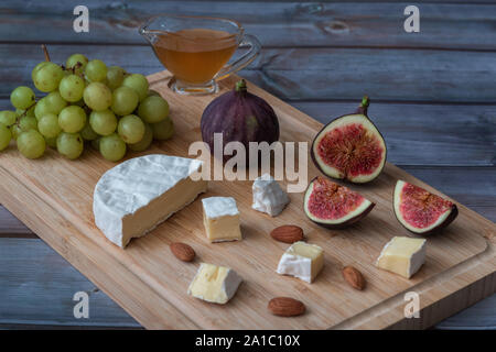 Dessert Häppchen zum Wein - Feigen, Brie Käse, grüne Weintrauben, Honig auf einem Holzbrett serviert. Stockfoto