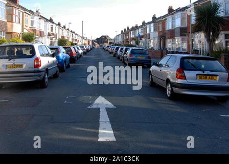 Weißer Pfeil in der Straße, der die Richtung des Reisen in schmalen Wohnstraße, one-way durch Autos eng auf beiden Seiten der Straße geparkt Stockfoto