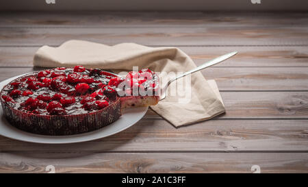 Torte mit Beeren: Himbeeren, Erdbeeren, Johannisbeeren, auf einem weissen Teller, neben einem Stück Kuchen auf der Schulter Stockfoto