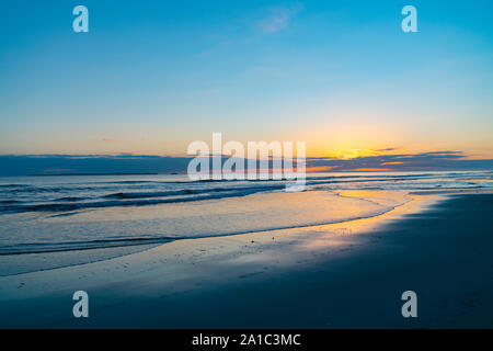 Oceanbeach als Sonne am Horizont erstellen goldenen Glanz über Meer zum Strand noch in dunklen von Morgen. Stockfoto