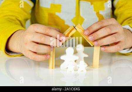 Junge bildet ein Dach mit Stücke Holz über zwei kleine Zeichen Stockfoto