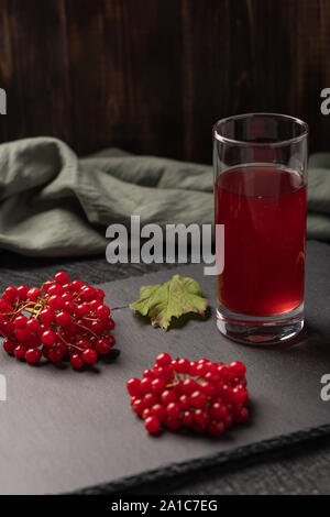 Rote Saft von viburnum in einem Glas auf einem dunklen Hintergrund. In der Nähe von viburnum Beeren, und Leinen. Gesunde Ernährung Stockfoto