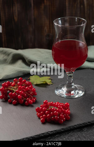 Rote Saft von viburnum in einem Glas auf einen Stamm auf einem dunklen Hintergrund. In der Nähe von viburnum Beeren und Bettwäsche Serviette. Gesunde Ernährung Stockfoto