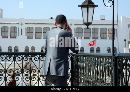 Eine junge tunesische Geschäftsmann in Anzug nimmt einen geschäftlichen Anruf auf seinem Handy auf einer Terrasse mit Blick auf die Medina von Tunis, Tunesien. Stockfoto