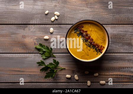 Hausgemachte Cremesuppe mit einer Mischung aus Bohnen mit rotem Pfeffer und schwarzem Sesam auf einer hölzernen Hintergrund. Petersilie und weißen Bohnen in der Nähe der Platte Stockfoto