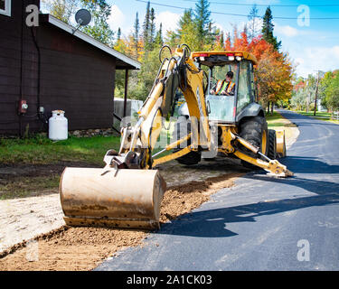 Ein mit Rädern Baggerlader bagger Glättung der Schulter und Kanten von einem Dorf Straße in Spekulant, NY, USA Stockfoto