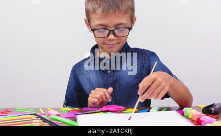 Banner Junge in ein blaues Hemd und Brille sitzt an einem Tisch auf einem weißen Hintergrund. Kreative Aktivitäten hobby zeichnen Stockfoto