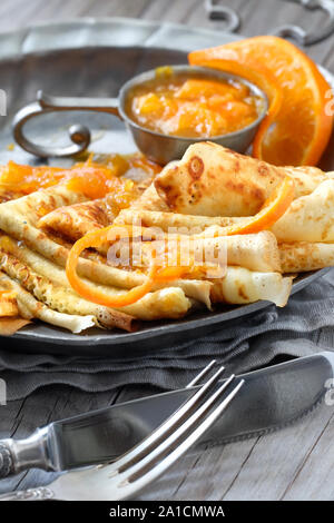 Crepes Suzette auf vintage Metallplatte auf Holztisch mit orange Sauce serviert, vertikale Nahaufnahme Stockfoto