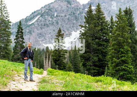 Albion Basin, Utah Pinien und Mann stehen auf Sommer dirt road Trail 2019 in Wasatch Mountains mit Rocky snowy Devil's Castle Mountain Stockfoto